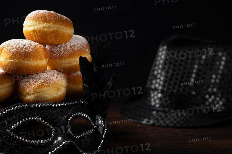 Doughnuts against a dark background next to a black hat and carnival mask