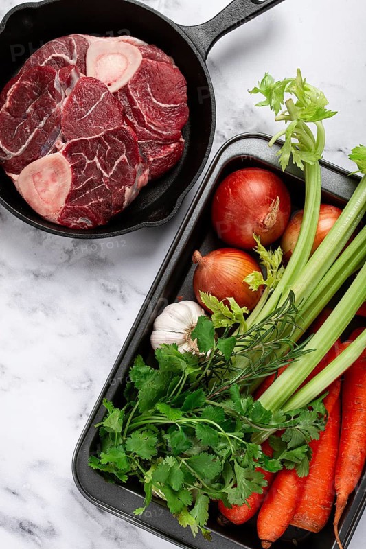 Sknuckle on the bone, raw meat for ossobuco, in a cast-iron pan, baking sheet with vegetables, top view, no people