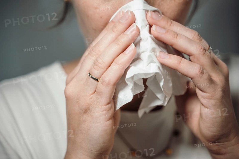 Woman holding a crumpled handkerchief to her nose, possibly with a cold or sneezing, 'symbolic image' cold