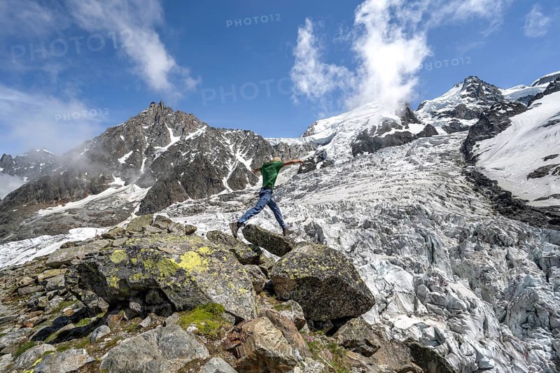 Mountaineer jumping from rock to rock, high alpine glaciated mountain landscape, La Jonction, Glacier des Bossons meets Glacier de Taconnaz, summit of Aiguille du Midi, Mont Maudit and Mont Blanc, Chamonix, Haute-Savoie, France, Europe