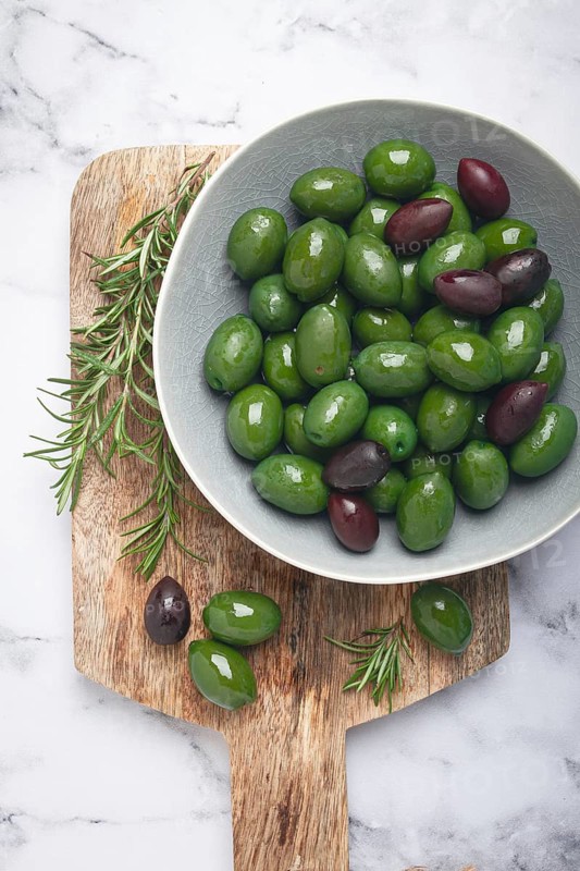 Chalkidiki olives, classic Greek green olives, in a bowl on a cutting board, top view, without people