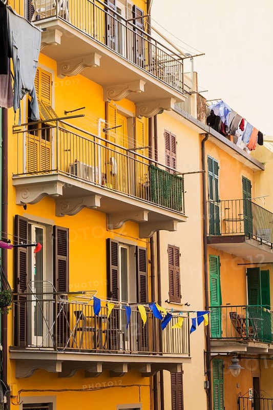 Yellow and beige stucco cladded residential apartment building facade and washed clothes drying on clothesline on balcony, Manarola, Cinque Terre, La Spezia province, Italy, Europe