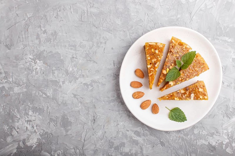 Traditional turkish candy cezerye made from caramelised melon, roasted walnuts, hazelnuts, pistachios on white ceramic plate on a gray concrete background. top view, flat lay, copy space