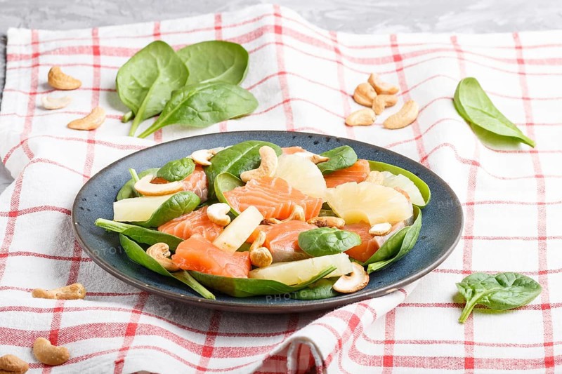 Fresh salmon with pineapple, spinach and cashew on a gray concrete background. Side view, linen tablecloth