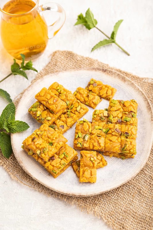 Traditional iranian dessert sohan with glass of green tea on a gray concrete background and linen textile. side view, close up, selective focus