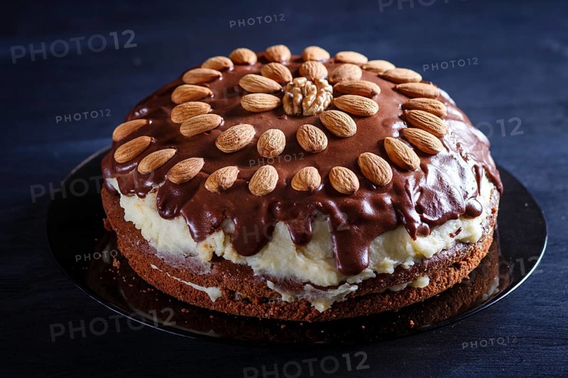 Homemade chocolate cake with milk cream and almonds on black wooden background. close up