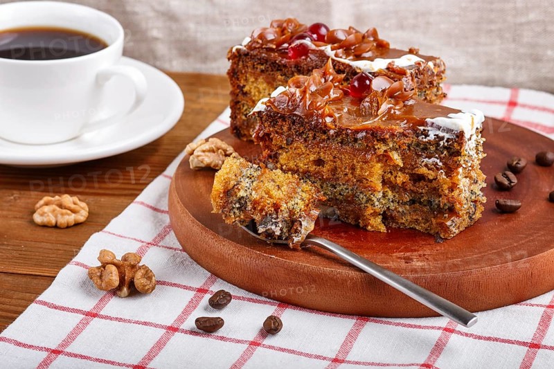 A piece of cake with caramel cream cutted with spoon on a wooden kitchen board and a cup of coffee, brown wooden background, close up