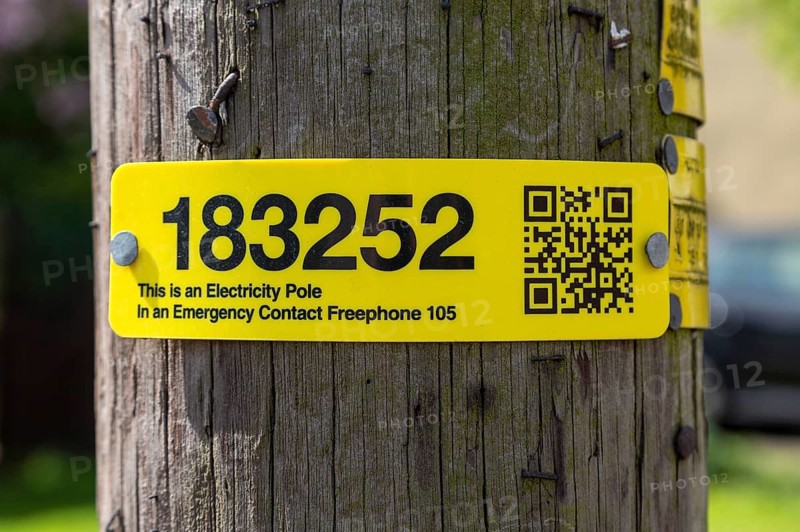Electricity pole yellow numbered identification tag with emergency contact freephone phone number UK