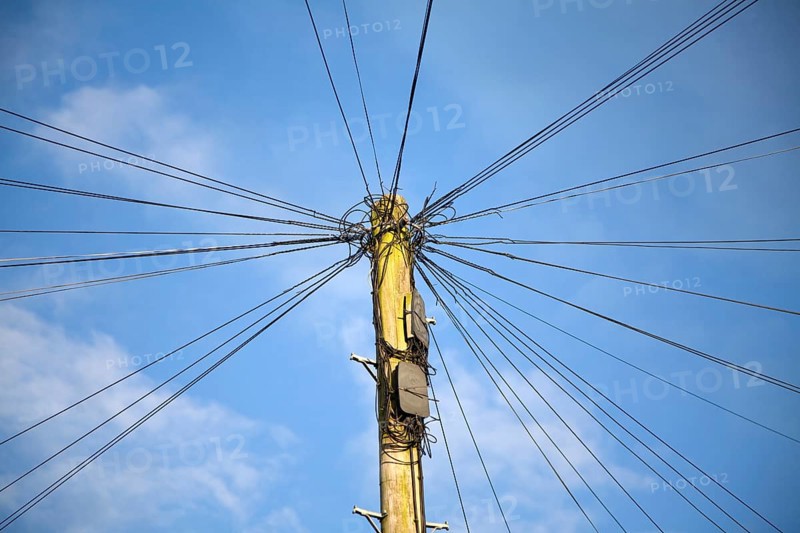 Telephone line cables radiating out fro telegraph pole against blue sky, UK