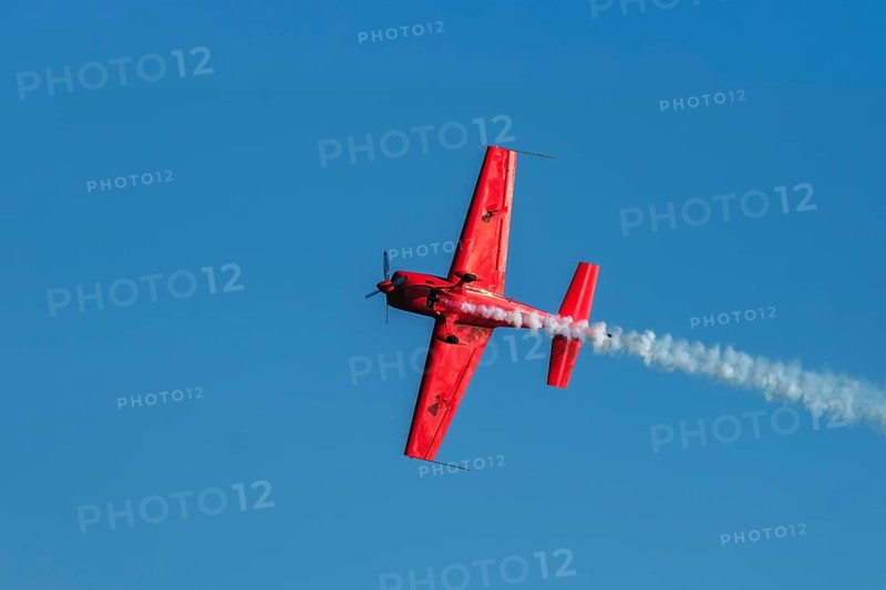 Red stunt aerobatic plane performing stunts in blue sky. Concept of speed, difficulty, precision, risk