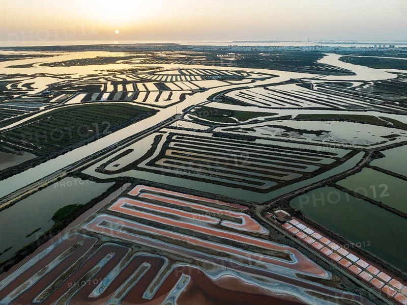 Saline ponds at the salt works near Chiclana de la Frontera. The orange-red colour depends on the level of salinity and is directly caused by the algae Dunaliella salina and brine shrimp. At sunset. Aerial view. Drone shot. Bahía de Cádiz Nature Reserve, Cádiz province, Andalusia, Spain, Europe
