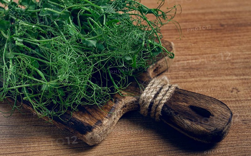 A rustic wooden cutting board holds a pile of fresh microgreens, showcasing vibrant colors and delicate textures in a cozy kitchen atmosphere, perfect for culinary creations.