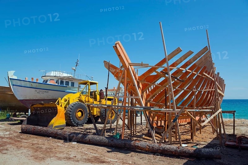 A ship under construction with a yellow excavator at a shipyard by the sea under a blue sky, Ierissos, Sithonia, Chalkidiki, Central Macedonia, Greece, Europe