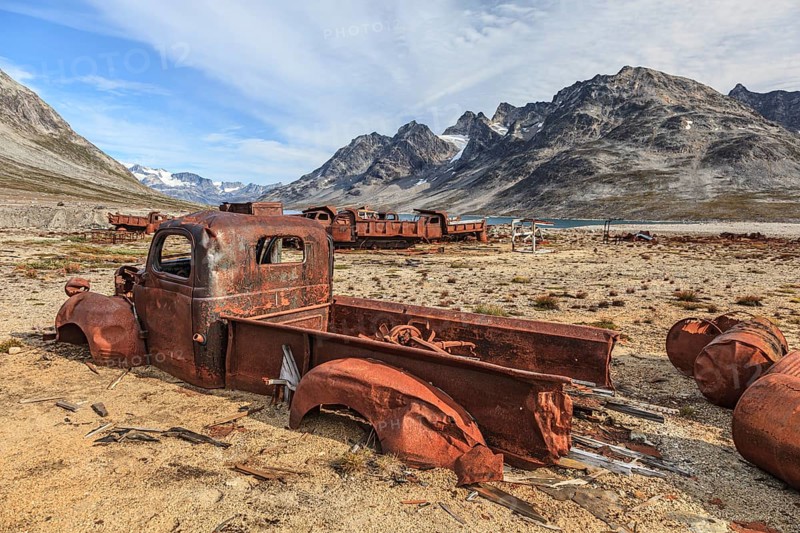 Rusted oil barrels and cars on a fjord in front of steep mountains, remains of a US airbase from the Second World War, Ikateq Fjord, East Greenland, Greenland, North America