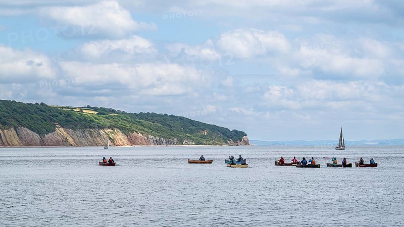 People in a canoe on Seaton Bay with the Haven Cliffs Naturist Beach in the background, Jurassic Coast, Seaton, Devon, England, United Kingdom, Europe