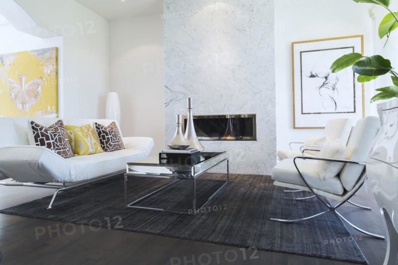 Living room with white leather and chrome sofa, armchairs, glass-top coffee table, gas fireplace with grey nuanced marble mantle-piece inside a luxurious residential home, Quebec, Canada, North America
