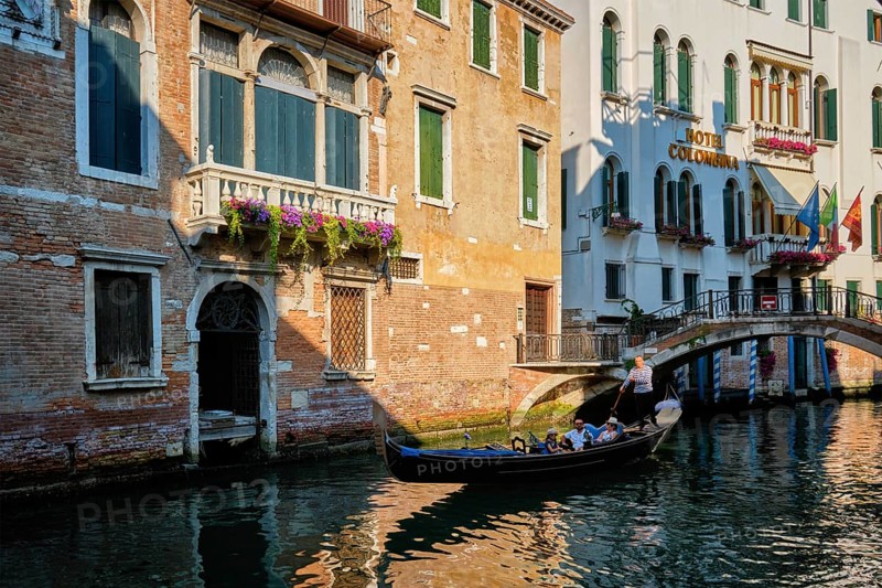VENICE, ITALY, JULY 19, 2019: Narrow canal between colorful old houses with gondola boat with tourists and gonolier in Venice, Italy, Europe