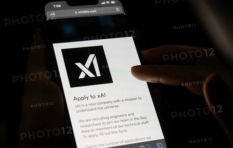 In this photo illustration, A person browses website of xAI, displayed on a mobile phone, Elon Musk images in the background screen, in Guwahati, India 0n 15 July 2023. Tesla CEO Elon Musk launches Artificial Intelligence company xAI on 12 July 2023, the company's goal is to understand the true nature of the universe