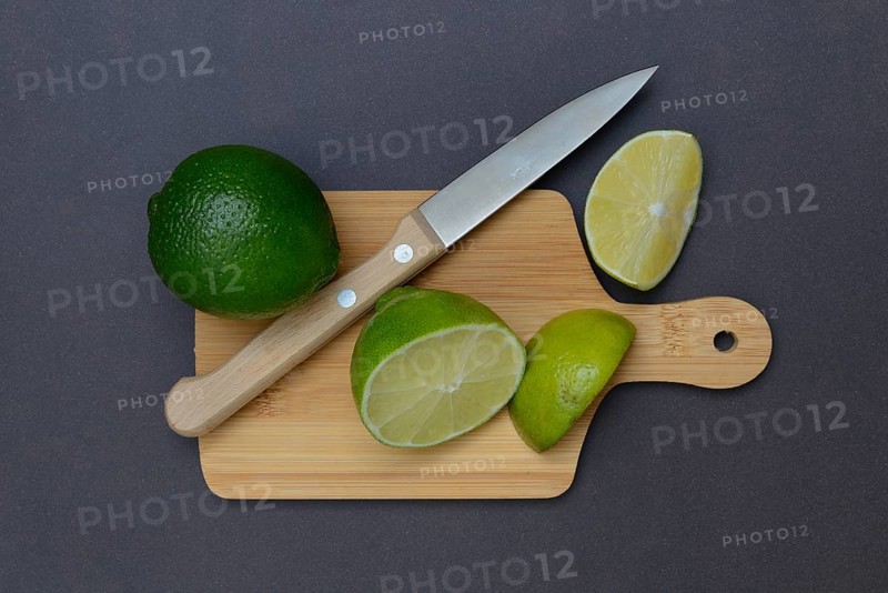 Halved limes on a chopping board with a kitchen knife