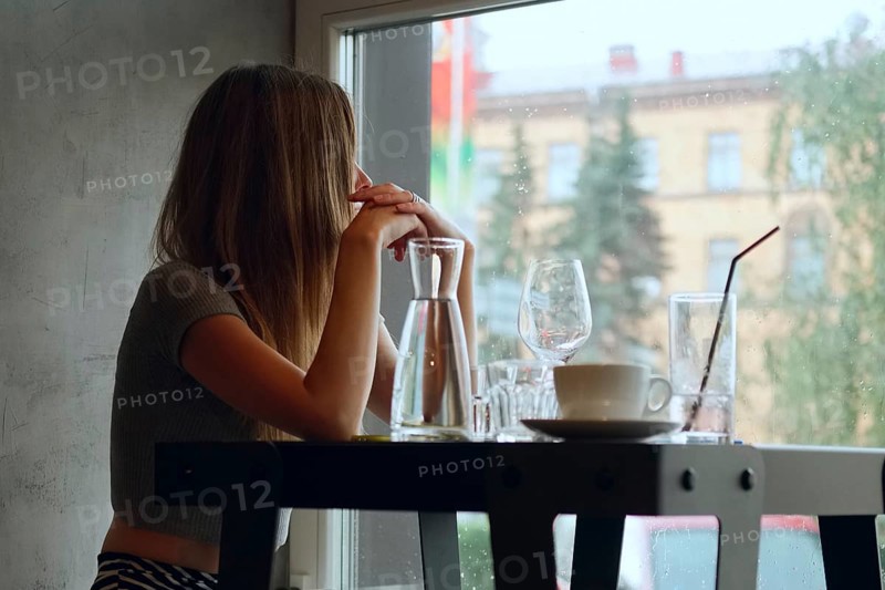 Soft focus portrait of pretty young girl behind the table with cold cocktail and wine glass. (Image taken at wide open aperture and contains little noise)