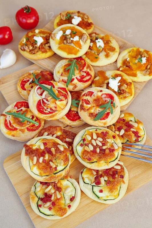 Swabian cuisine, mini dinnete, also dennete, dinnede, denetle on wooden boards, hearty, salty, yeast pastry topped with vegetables, tomatoes, pumpkin, courgette slices, sour cream, grated cheese, pine nuts, healthy, yeast yeast dough, vegetarian, bake, out of the oven, typical Swabian reinterpreted, party pastry, finger food, snacks for on the go, tomatoes in the back, garlic, traditional cuisine, food photography, studio, Germany, Europe
