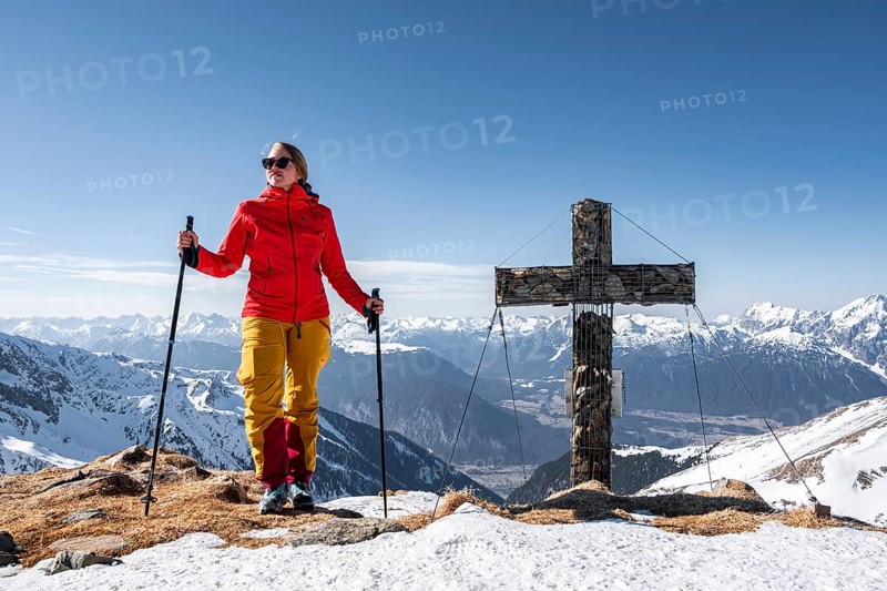 Ski tourer standing next to summit cross, summit of Mitterzeigerkogel in winter, Sellraintal, Kühtai, Tyrol, Austria, Europe