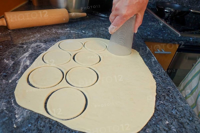 Swabian cuisine, preparation of mini dinnete, also dennete, dinnede, dennetle, hearty, salty, cutting out yeast dough blanks with glass, raw yeast dough, yeast pastry, baking, out of the oven, typical Swabian reinterpreted, party pastry, finger food, appetisers for on the go, traditional cuisine, man's hand, rolling pin at the back, worktop, food photography, studio, Germany, Europe