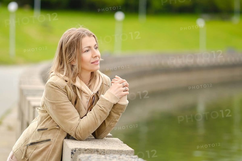 Close up of smiling middle aged woman with a wistful look standing by the river embankment in city park