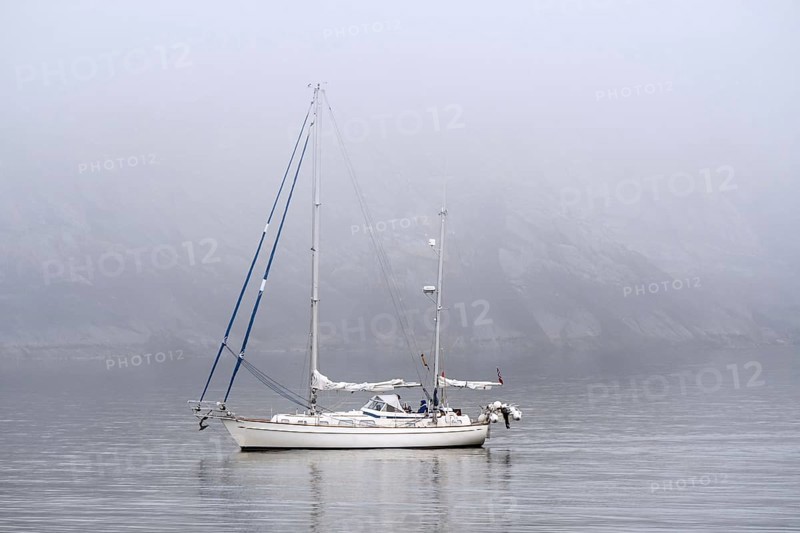 Sailboat, sailing boat, yacht with lowered sails at sea during bad visibility due to thick fog, dense mist