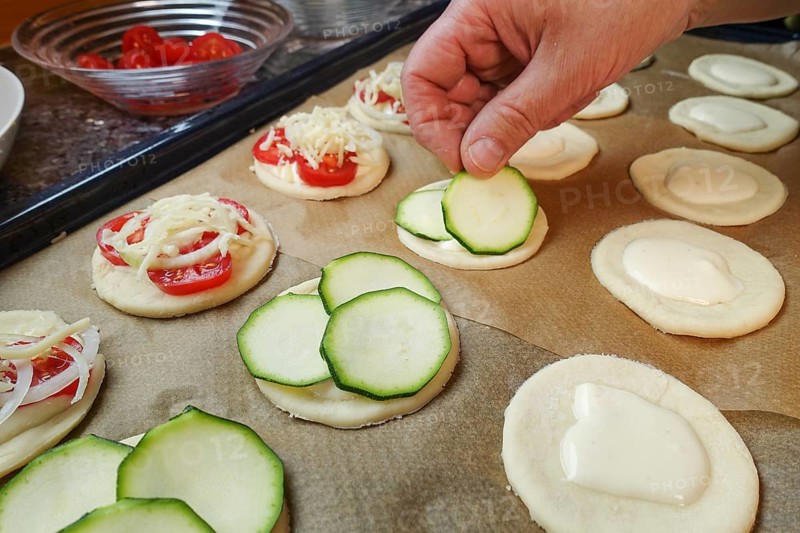 Swabian cuisine, preparation of mini dinnete, also dennete, dinnede, dennetle, hearty, salty, topping raw yeast yeast dough with courgette slices, tomatoes, vegetables, sour cream, yeast pastry, vegetarian, bake, out of the oven, typical Swabian reinterpreted, party pastry, finger food, snacks for on the go, traditional cuisine, baking paper, oven tray, man's hand, food photography, studio, Germany, Europe