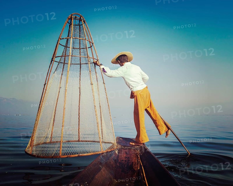 Vintage retro effect filtered hipster style image of Myanmar travel attraction. Traditional Burmese fisherman with fishing net at Inle lake famous for their distinctive one legged rowing style