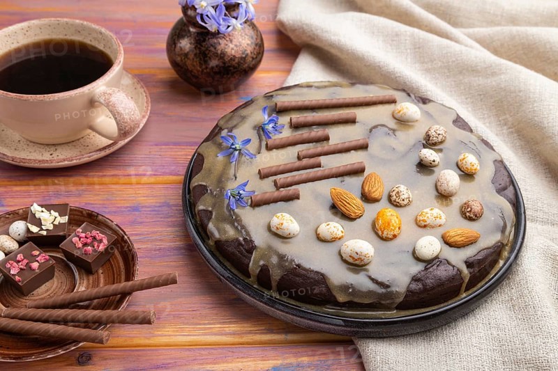 Homemade chocolate brownie cake with caramel cream and almonds with cup of coffee on a colored wooden background and linen textile. Side view, close up