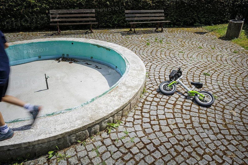 Symbolic photo on the subject of childhood loneliness, taken in the small town of Ziegenrück in Thuringia. A balance bike lies on a deserted square next to a switched-off fountain. Ziegenrück, 23.07.2024