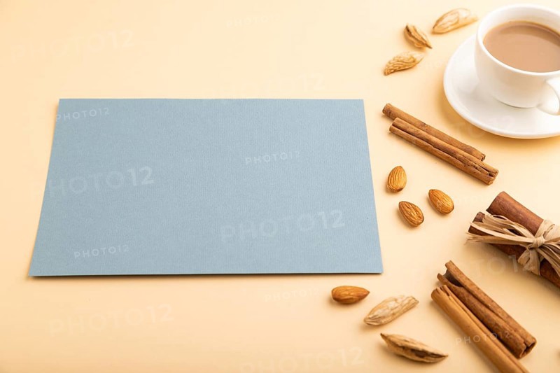 Composition with gray paper sheet, almonds, cinnamon and cup of coffee. mockup on orange background. Blank, side view, still life, copy space