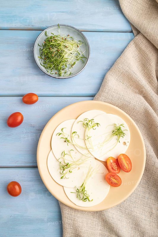 White cheese with tomatoes and cilantro microgreen on blue wooden background and linen textile. top view, flat lay, close up