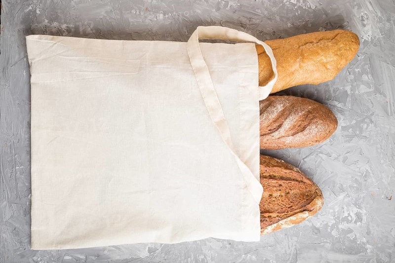 Reusable textile grocery bag with fresh baked bread on a gray concrete background. top view, flat lay, copy space. zero waste concept