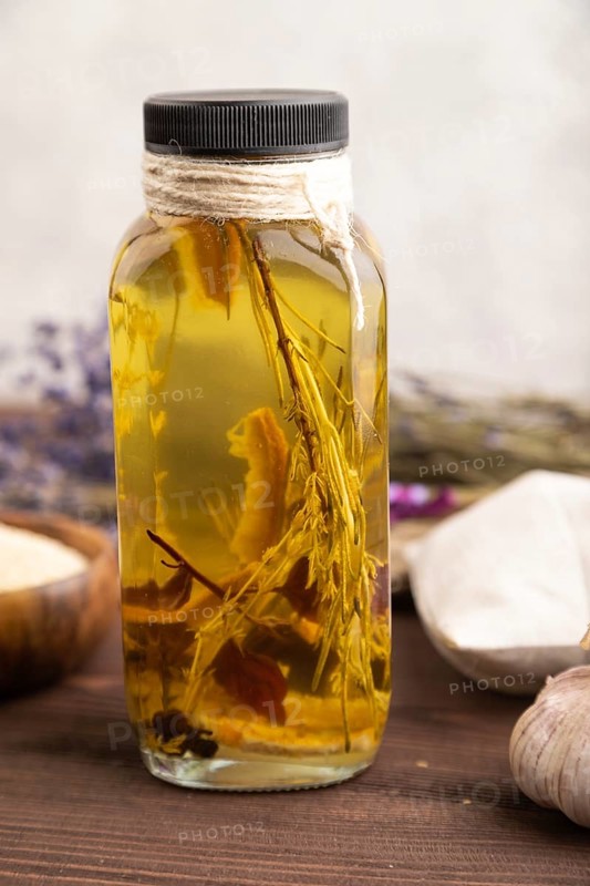 Sunflower oil in a glass jar with various herbs and spices, lavender, sesame, rosemary on a brown wooden background. Side view, close up