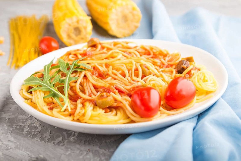 Corn noodles with tomato sauce and arugula on a gray concrete background and blue textile. Side view, close up, selective focus
