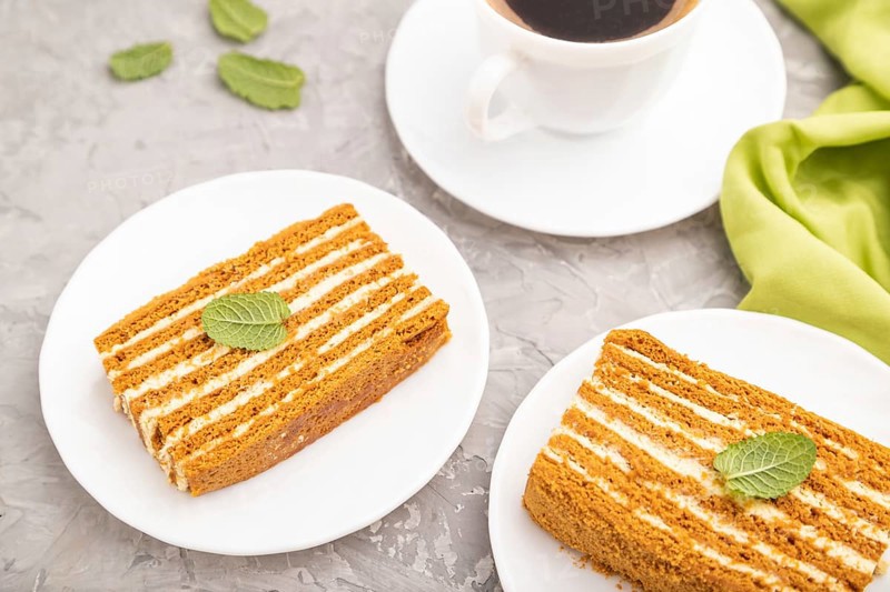 Homemade honey cake with milk cream and mint with cup of coffee on a gray concrete background and green textile. Side view, close up, selective focus