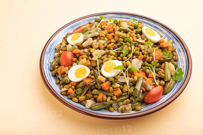 Mung bean porridge with quail eggs, tomatoes and microgreen sprouts on a pastel orange background. Side view, close up