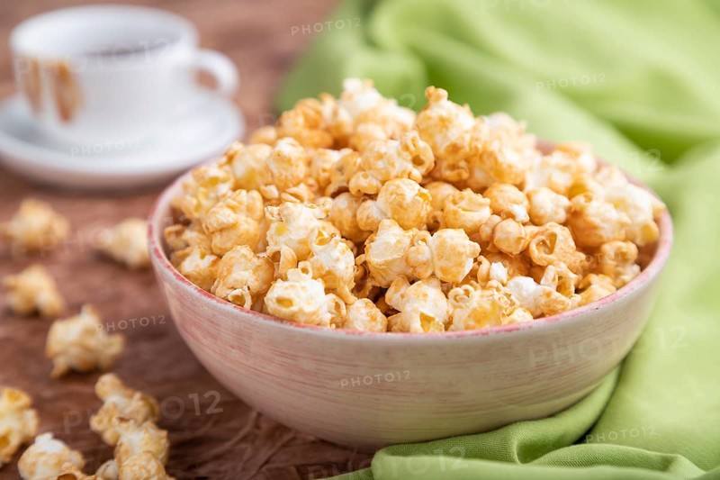 Popcorn with caramel in ceramic bowl on brown concrete background and green textile. Side view, close up, selective focus