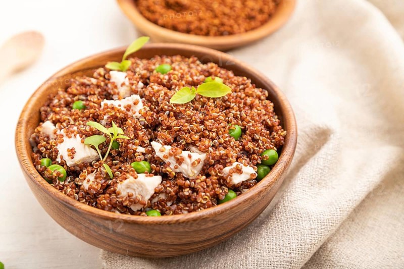 Quinoa porridge with green pea and chicken in wooden bowl on a white wooden background and linen textile. Side view, close up, selective focus