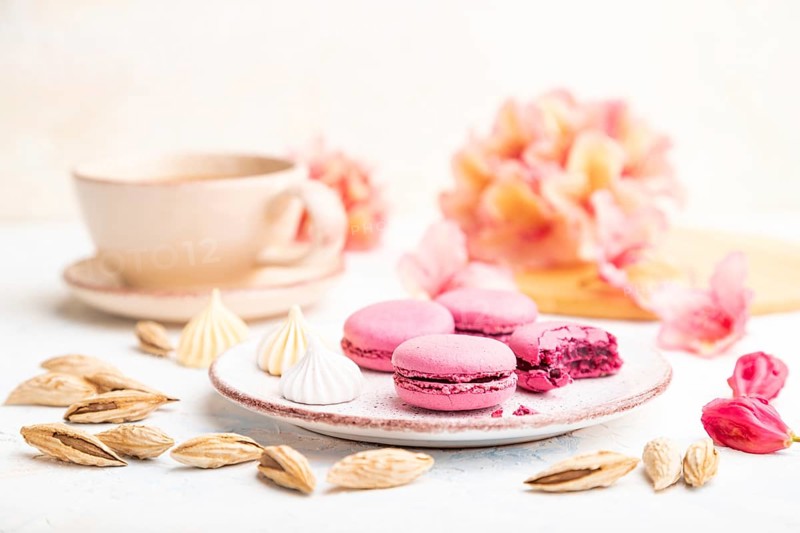 Purple macarons or macaroons cakes with cup of coffee on a white concrete background decorated with flowers. Side view, close up, selective focus