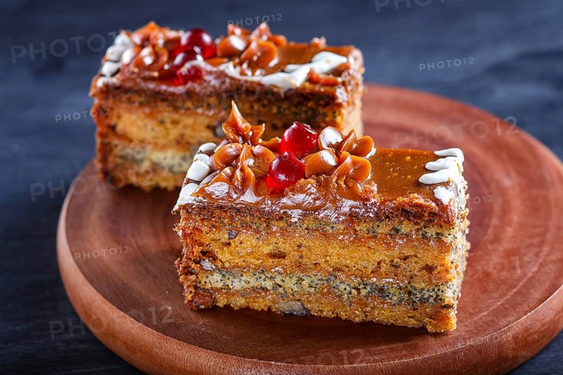 A piece of cake with caramel cream and poppy seeds on a wooden kitchen board. close up, selective focus, black background