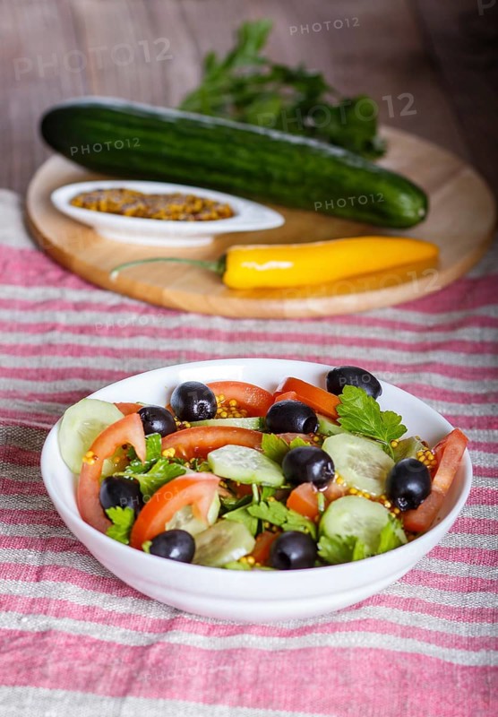 Vegetarian salad of tomatoes, cucumbers, parsley, olives and mustard on linen tablecloth, close up, selective focus