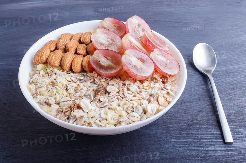A plate with muesli, almonds, pink grapes on a black wooden background. close up