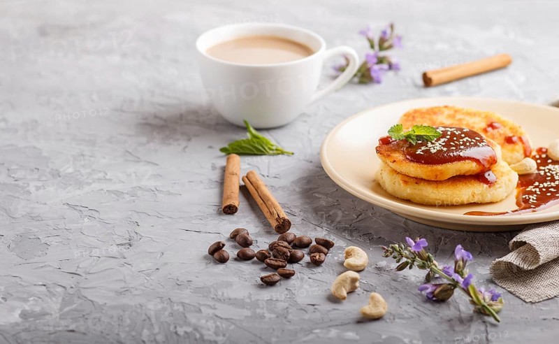 Cheese pancakes with caramel sauce on a beige ceramic plate and a cup of coffee on a gray concrete background. side view, close up