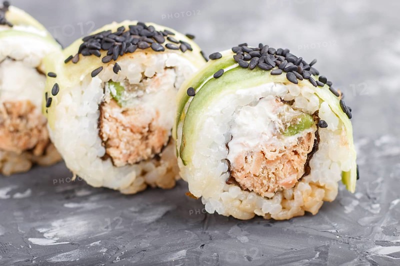 Japanese maki sushi rolls with tuna, cucumber, black sesame, cheese on black concrete background. Side view, close up, macro