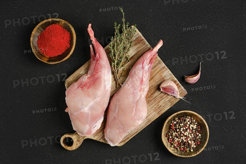 Two whole rabbit legs sit on a wooden cutting board alongside garlic, fresh thyme, and bowls of spice blends. This setup highlights an inviting environment for meal preparation.