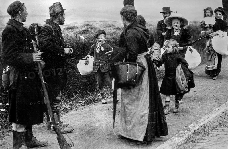 Two WWI Belgian foot-soldiers looking at families with children fleeing their city on foot during the beginning of World War One in 1914, Belgium, Europe